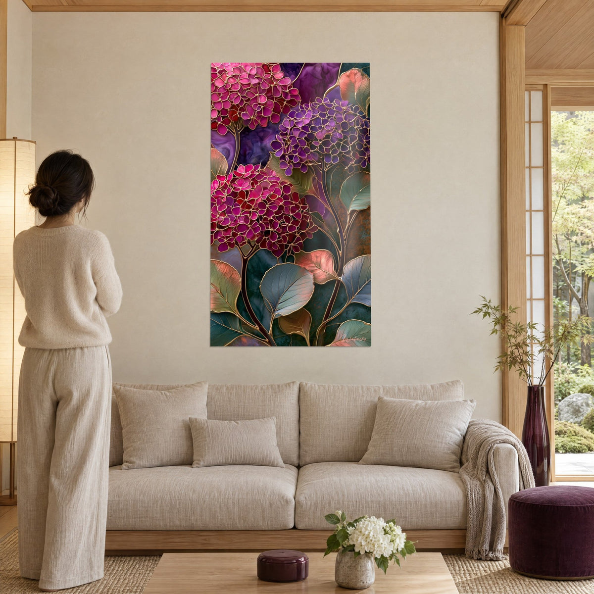 Gemälde mit magentafarbenen und violetten Hortensien, goldgerahmt im Glasmalerei-Stil, Frau von hinten, über einem Sofa in einem hellen Wohnzimmer