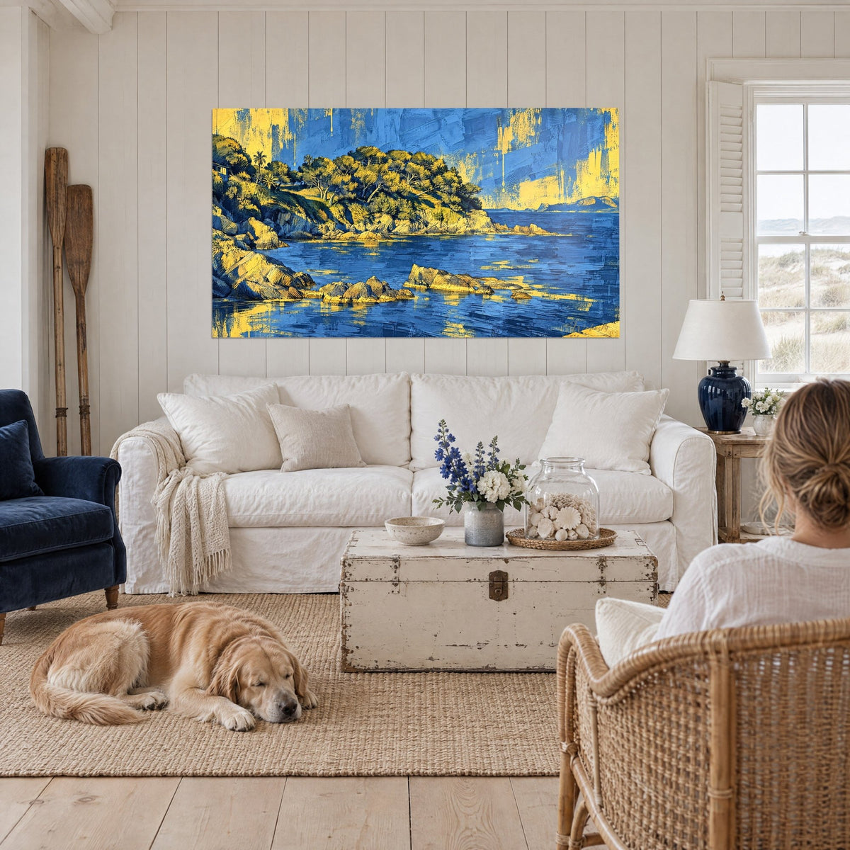Quadro cala rocciosa in blu oltremare e giallo dorato, pini sulla punta, retriever sdraiato, sopra un divano in un soggiorno luminoso