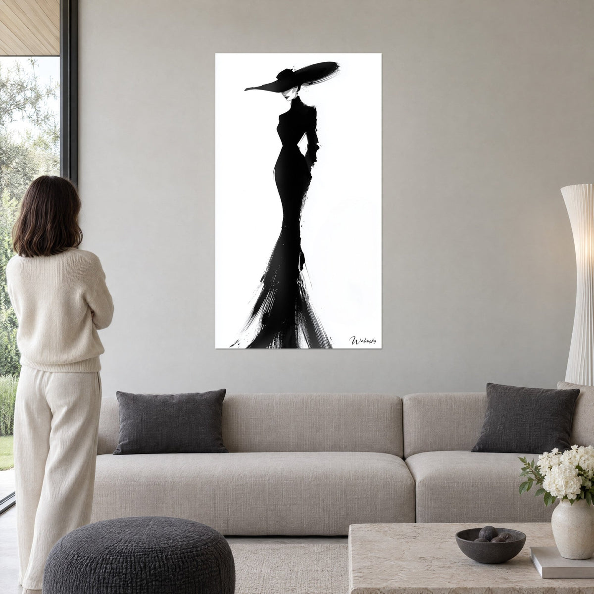 Tableau silhouette féminine en robe longue noire et chapeau à large bord sur fond blanc, au-dessus d'un canapé dans un salon lumineux