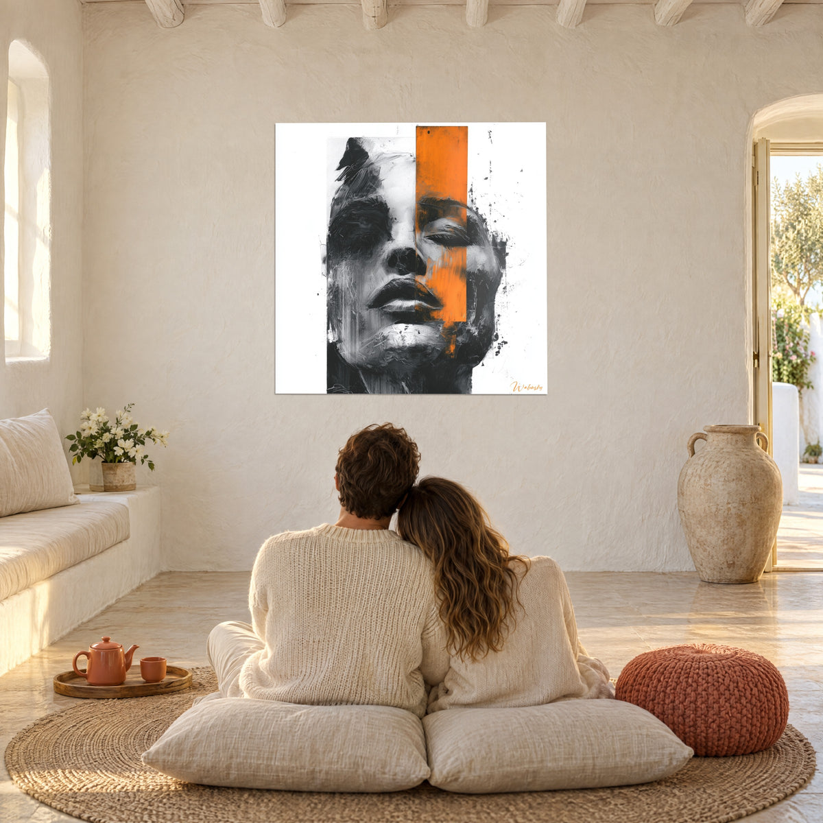 Quadro maschera femminile scolpita in grigio, nero e arancione, di fronte a una coppia seduta su cuscini in un salotto bianco