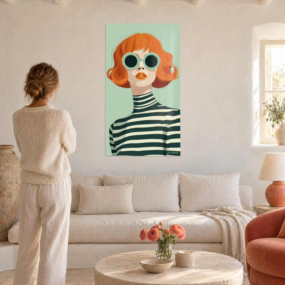 Quadro donna dai capelli rossi con caschetto mosso e occhiali rotondi verde menta, maglione a righe verde abete, sfondo verde acqua, sopra un divano in un soggiorno luminoso