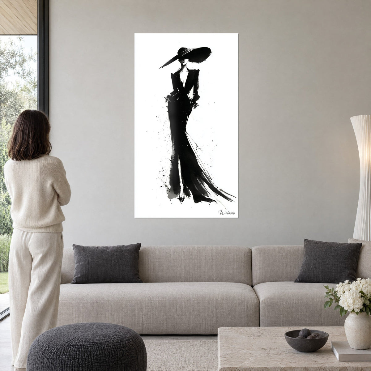 Tableau silhouette féminine au chapeau XXL, encre noire sur fond blanc, traînée éclaboussée, au-dessus d'un canapé dans un salon lumineux