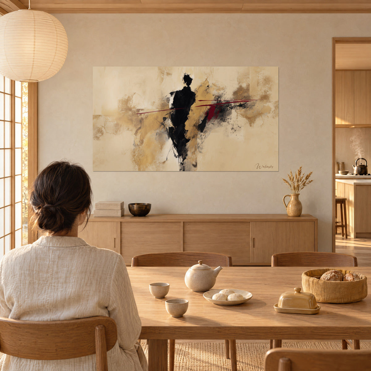 Wall art abstract walker in black ink blots and dark red streaks on golden beige, woman seen from behind seated at a table, Japandi home