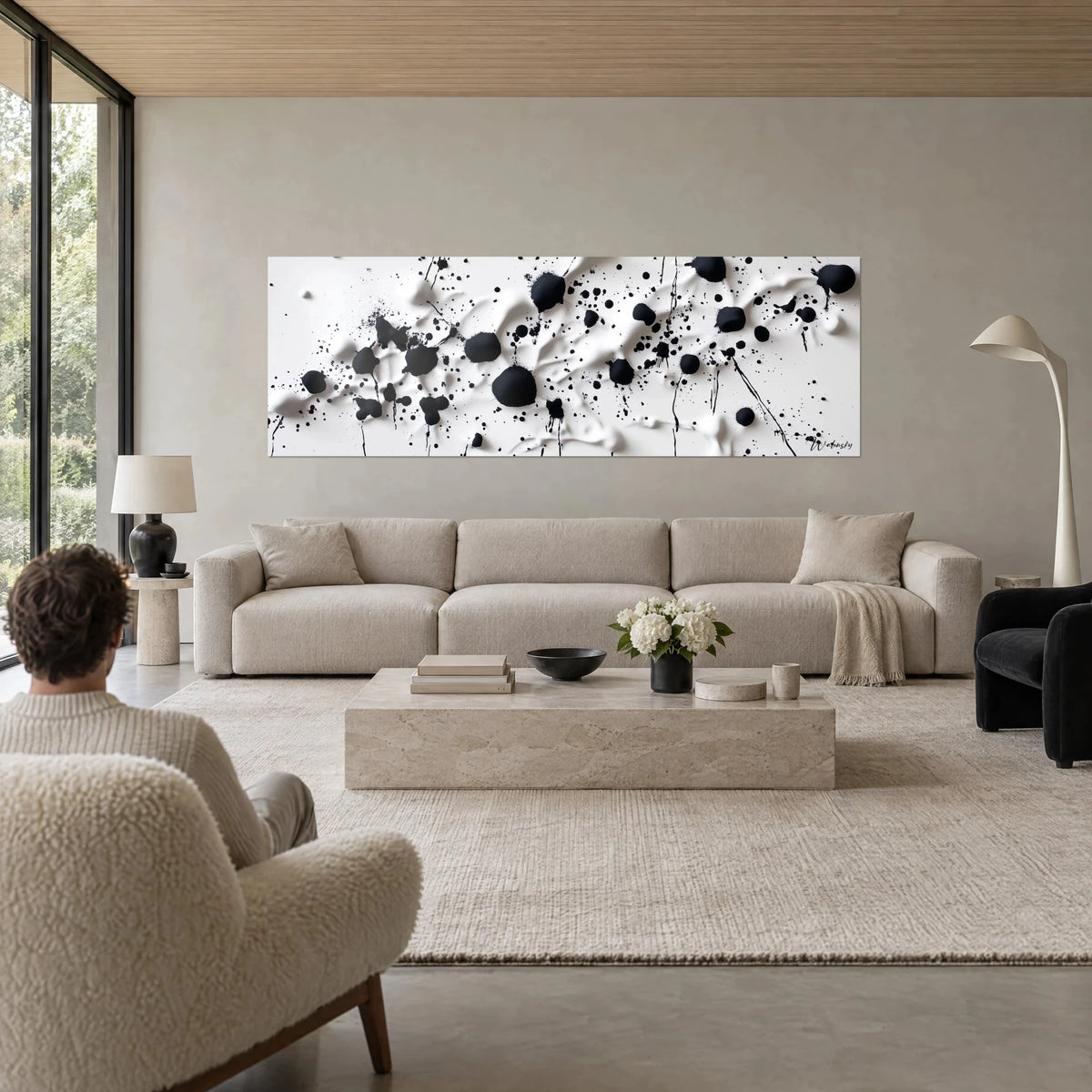 Wall art with black ink splashes on creamy white relief, panoramic, above a sofa in a bright living room