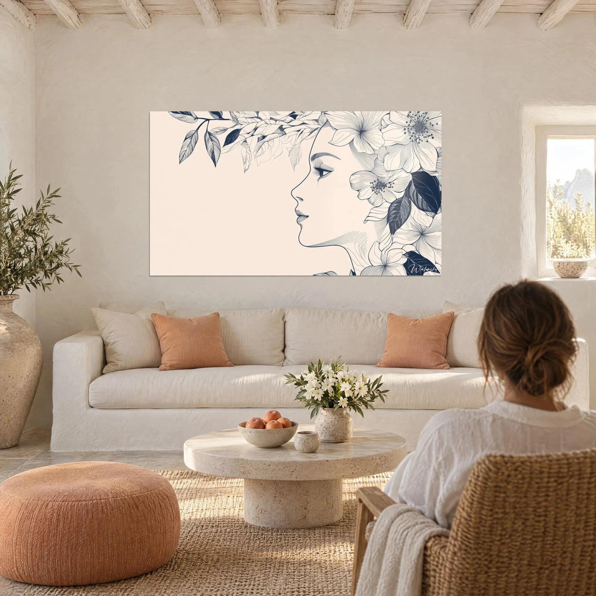 Tableau profil de femme couronnée de fleurs, encre bleu nuit sur fond rose pâle, au-dessus d'un canapé dans un salon lumineux