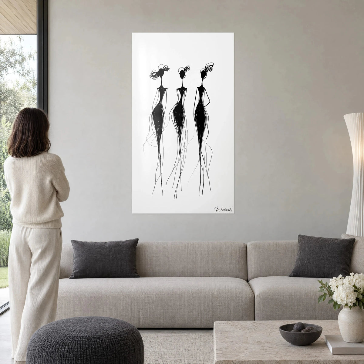 Tableau trois silhouettes noires filiformes sur fond blanc, chignons en boucles, femme de dos, au-dessus d'un canapé dans un salon lumineux