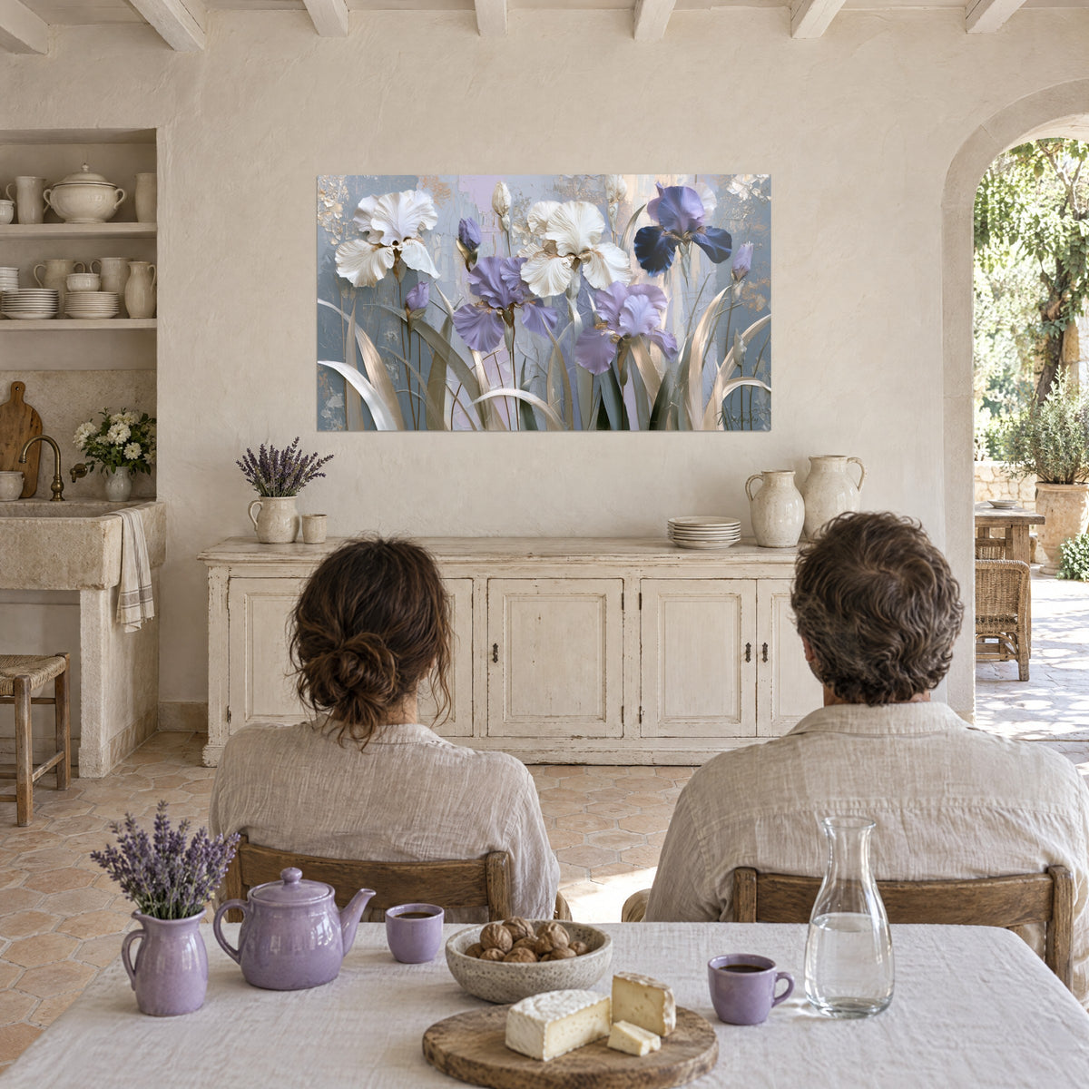 Cuadro de un jardín de iris púrpura y crema pintado con espátula, follaje gris verdoso, frente a una pareja sentada a la mesa de la cocina del mas