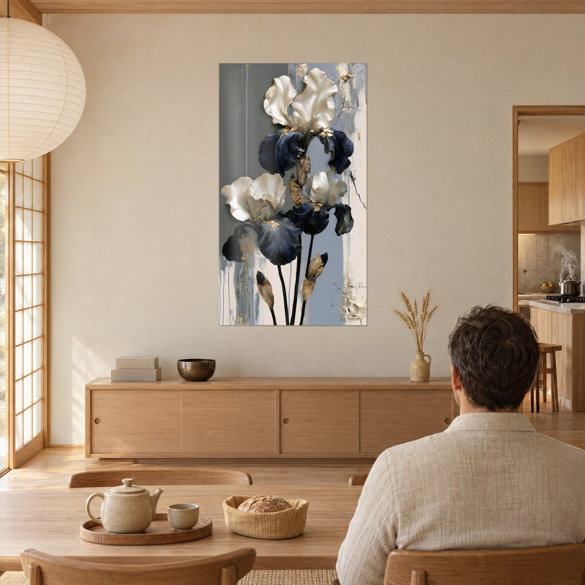 Cuadro tres iris con pétalos blancos satinados y azul marino, tallos negros, fondo gris fluido, hombre de espaldas a la mesa en un salón japandi