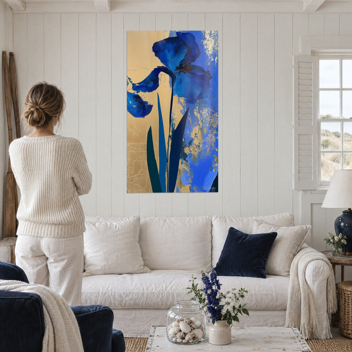 Wall art with royal blue iris, crumpled petals on a cracked gold background, a person seen from behind, hung above a sofa in a bright living room