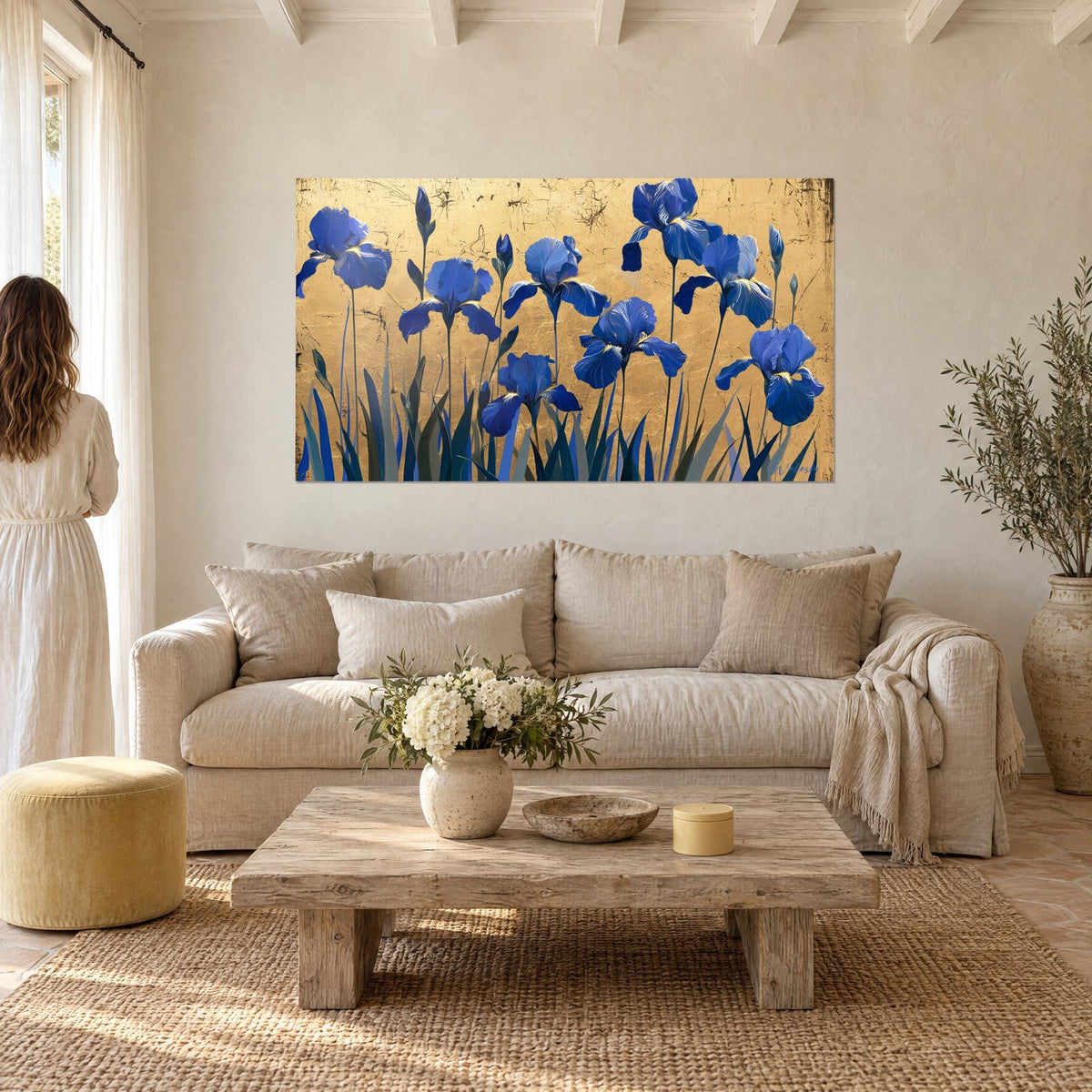 Wall art of a row of cobalt irises with crumpled petals on cracked gold leaf, couple seen from behind, above a sofa in a bright living room