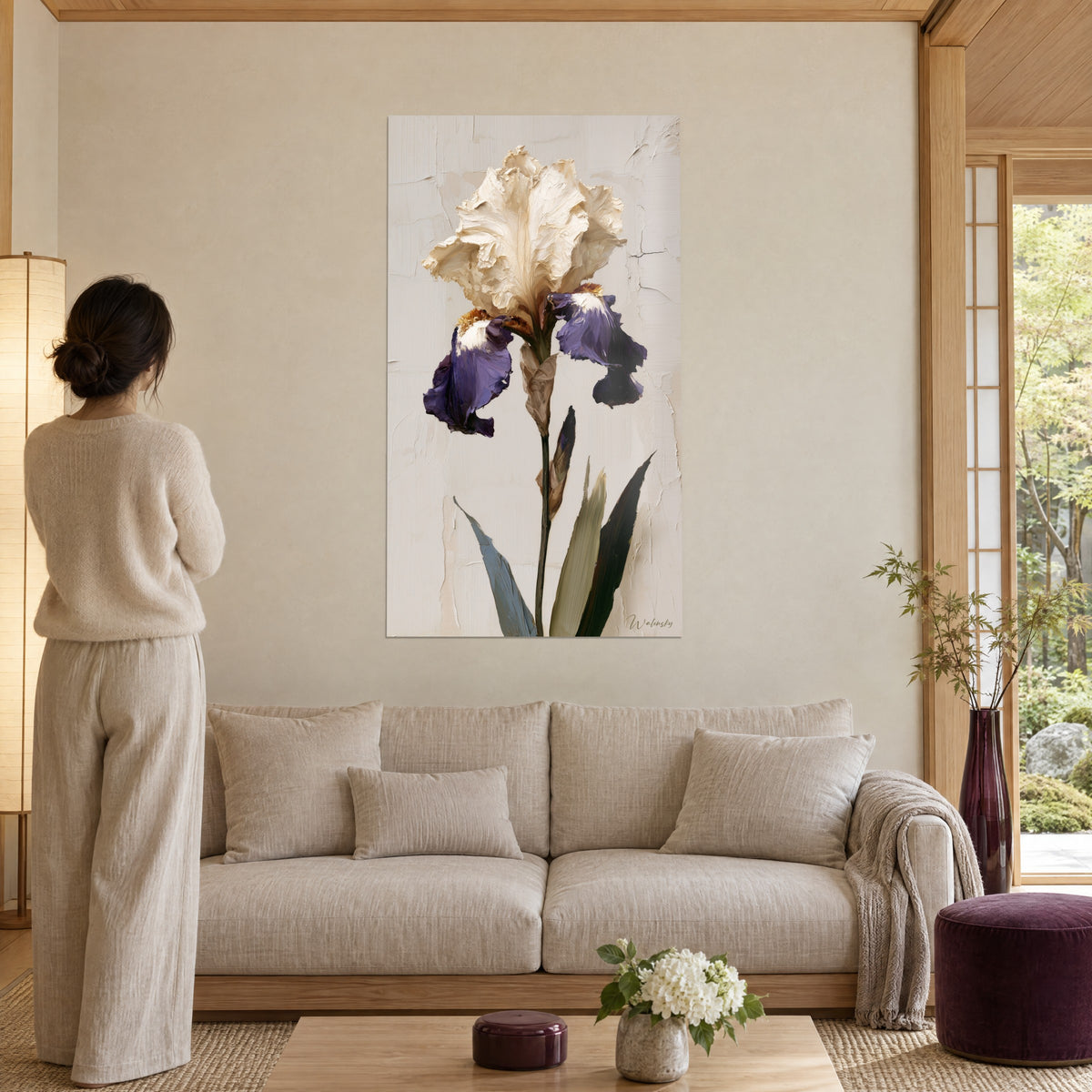 Wall art of an ivory iris with crumpled petals, green stems on a cracked beige background, above a sofa in a bright living room