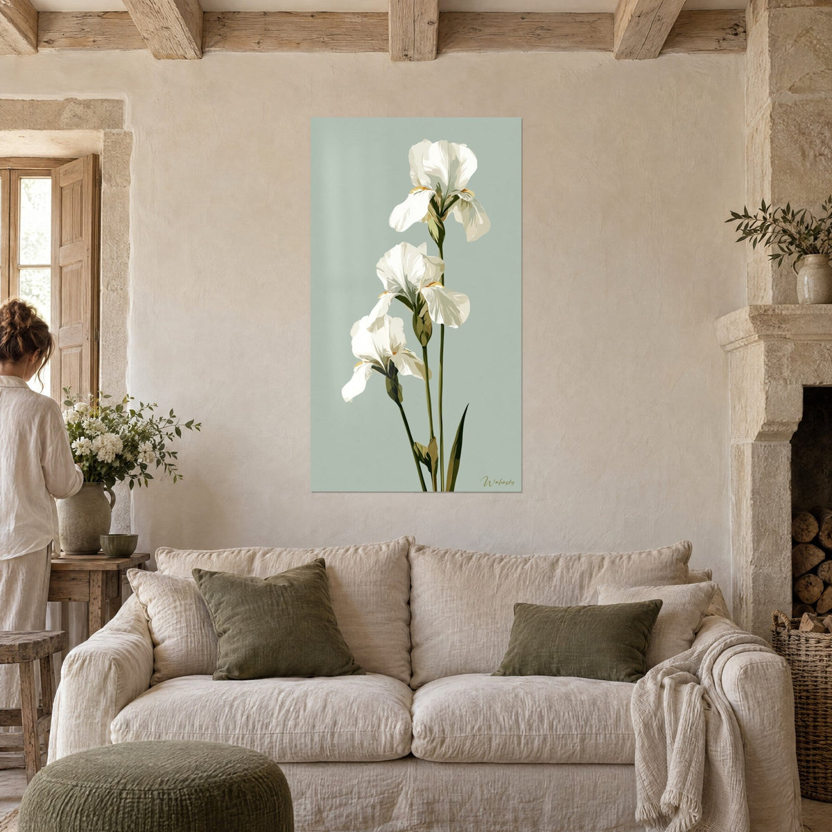 Wall art three white irises with upright stems on a almond green background, person seen from behind, above a sofa in a bright living room