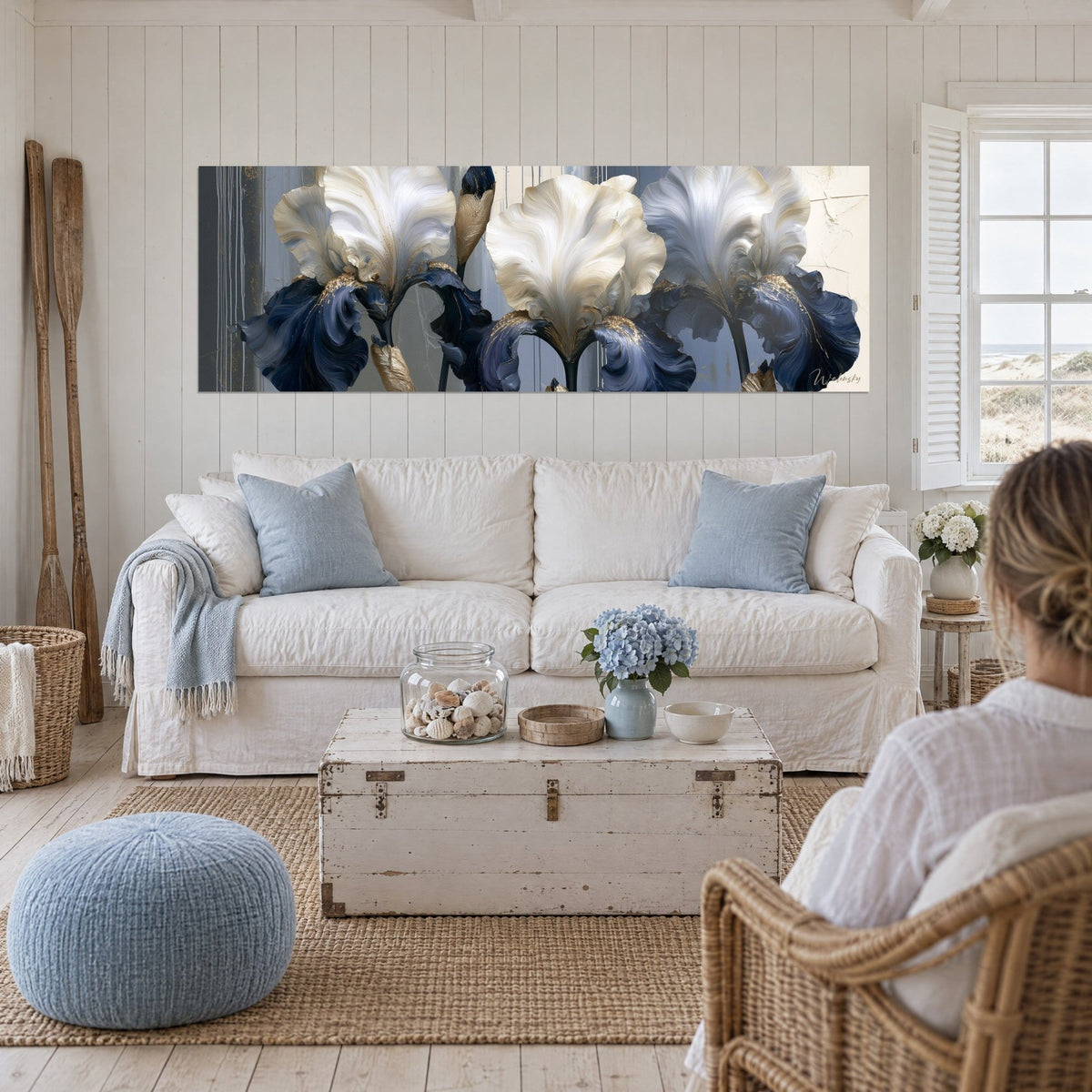 Quadro con tre iris color crema dai petali ondulati e petali blu navy punteggiati d'oro, sopra un divano in un soggiorno luminoso