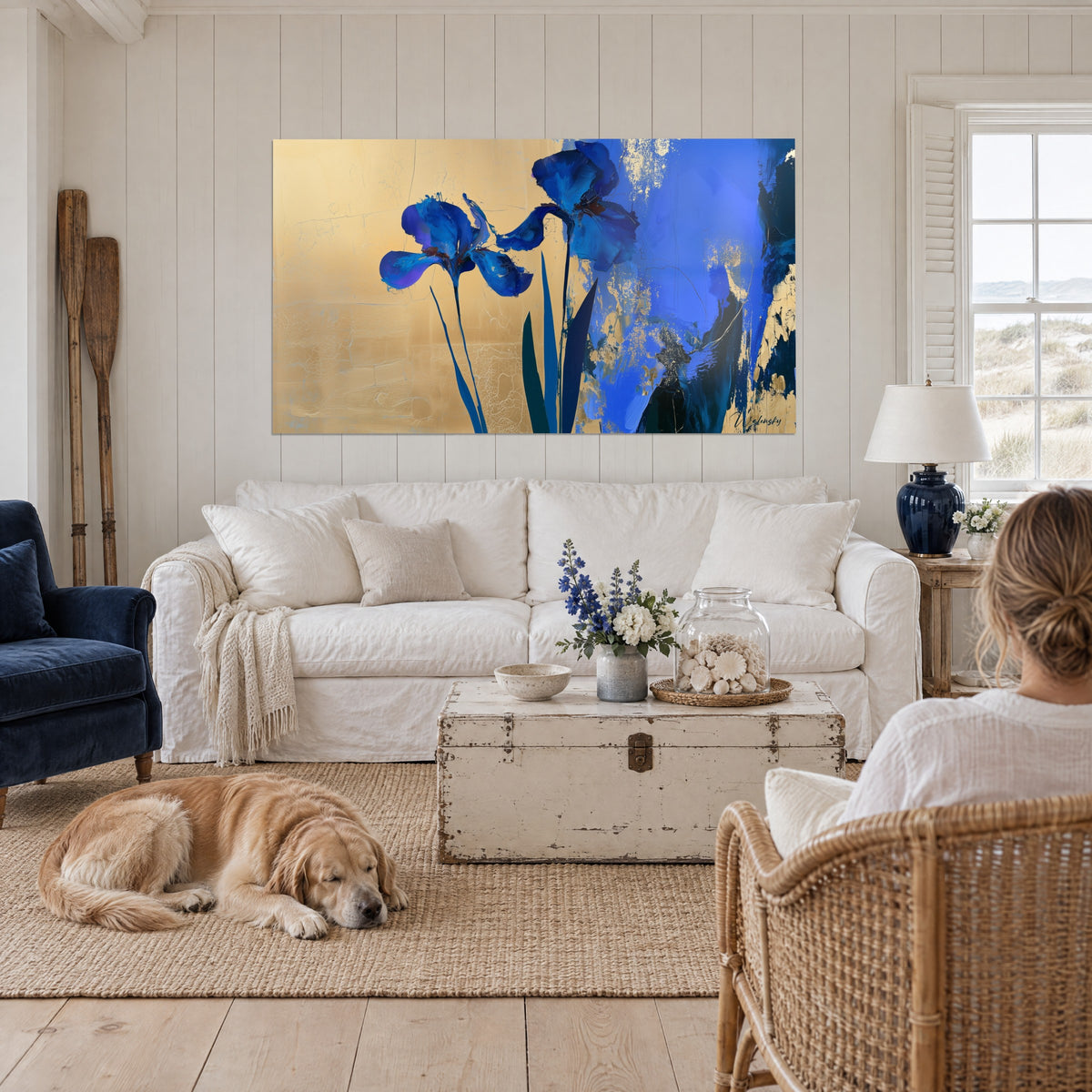 Tableau deux iris indigo sur fond d'or craquelé, retriever couché et personne de dos, au-dessus d'un canapé dans un salon lumineux