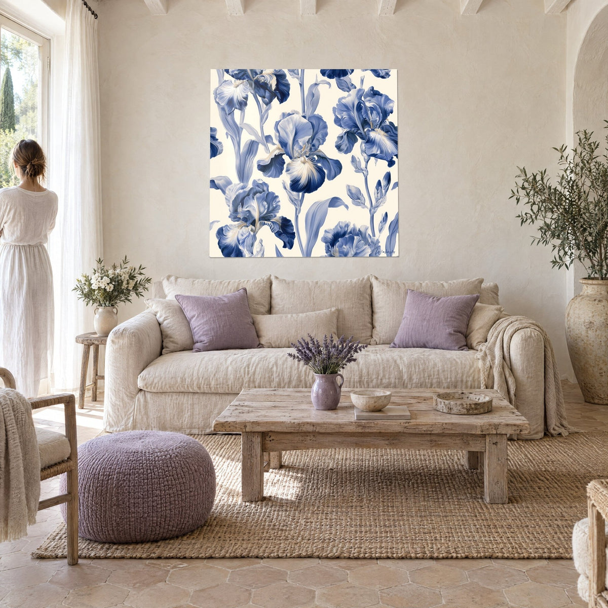 Quadro di iris barbuti blu notte dai petali ondulati su fondo avorio, appeso da una donna di spalle, sopra un divano in un soggiorno luminoso