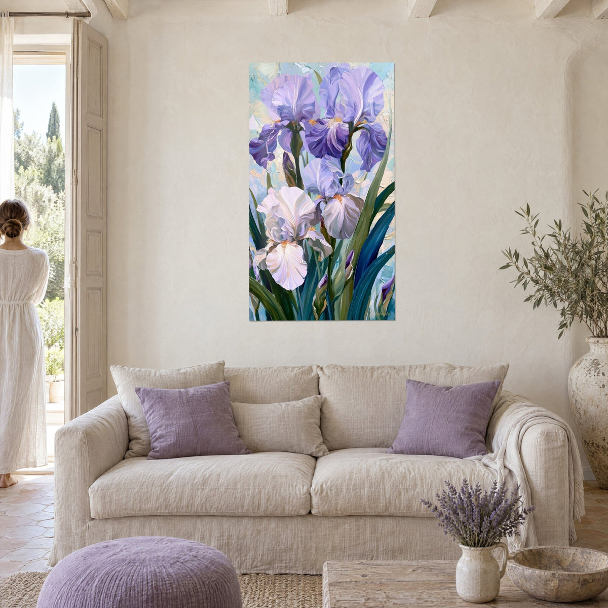 Wall art with mauve irises with crumpled petals and pearly white iris, teal leaves, woman seen from behind, above a sofa in a bright living room