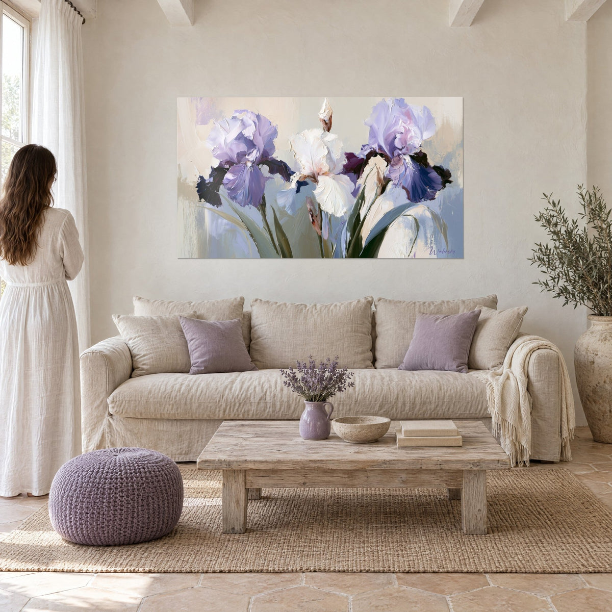 Wall art irises in lilac and white with crumpled petals, grey-green stems, woman in a white dress seen from behind, above a sofa in a bright living room
