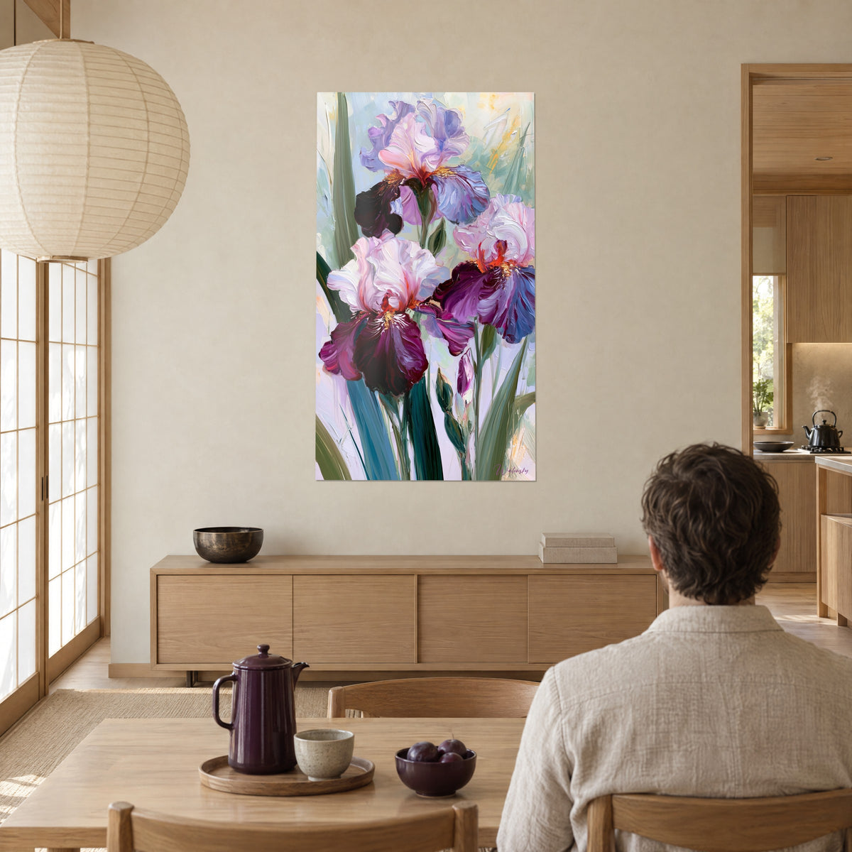 Schilderij irisboeket in pruimkleur en lavendelblauw met parelmoerachtige glans, tegenover een man aan tafel bij een groot raam