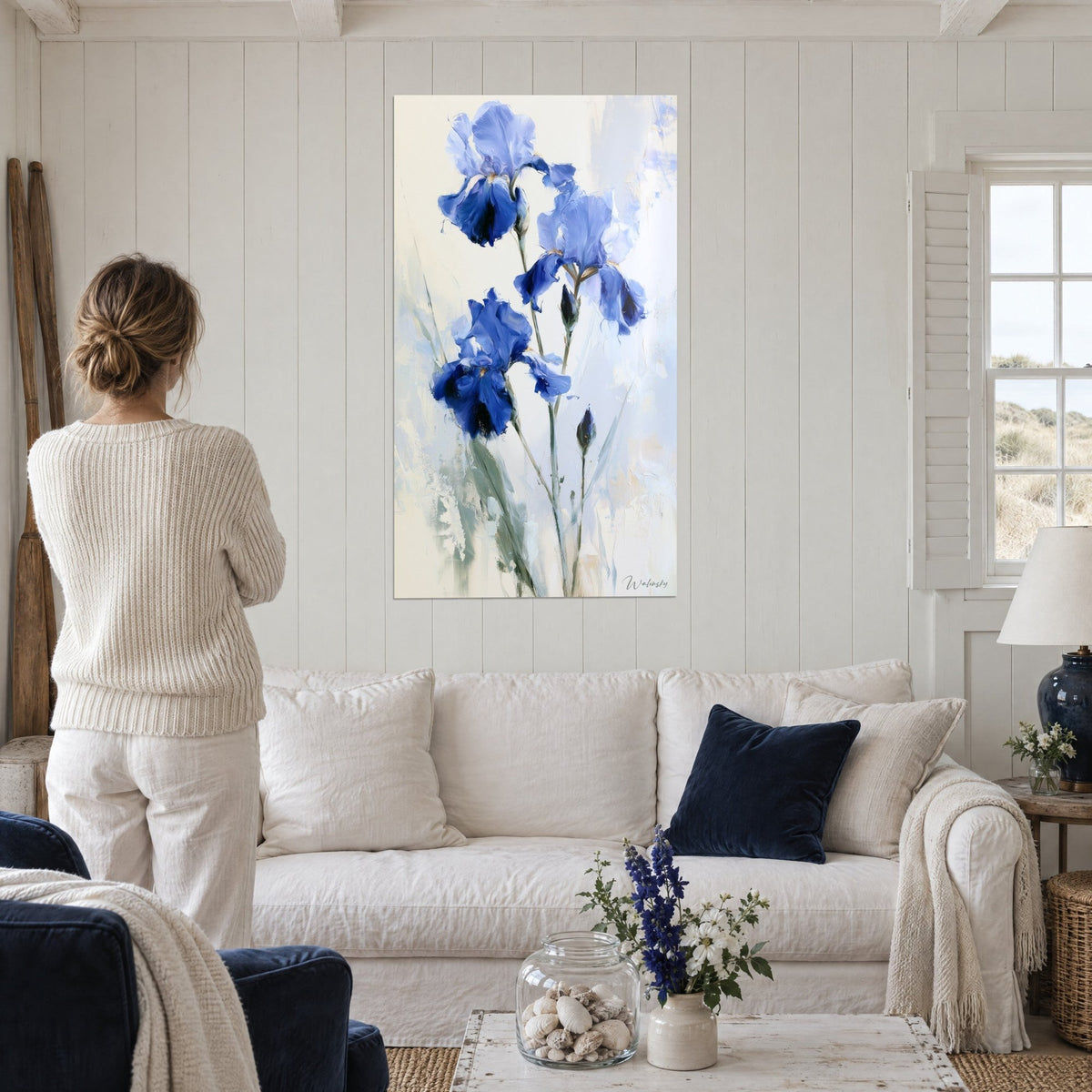 Wall art of cobalt blue iris with ivory petals, woman seen from behind above a sofa in a bright living room