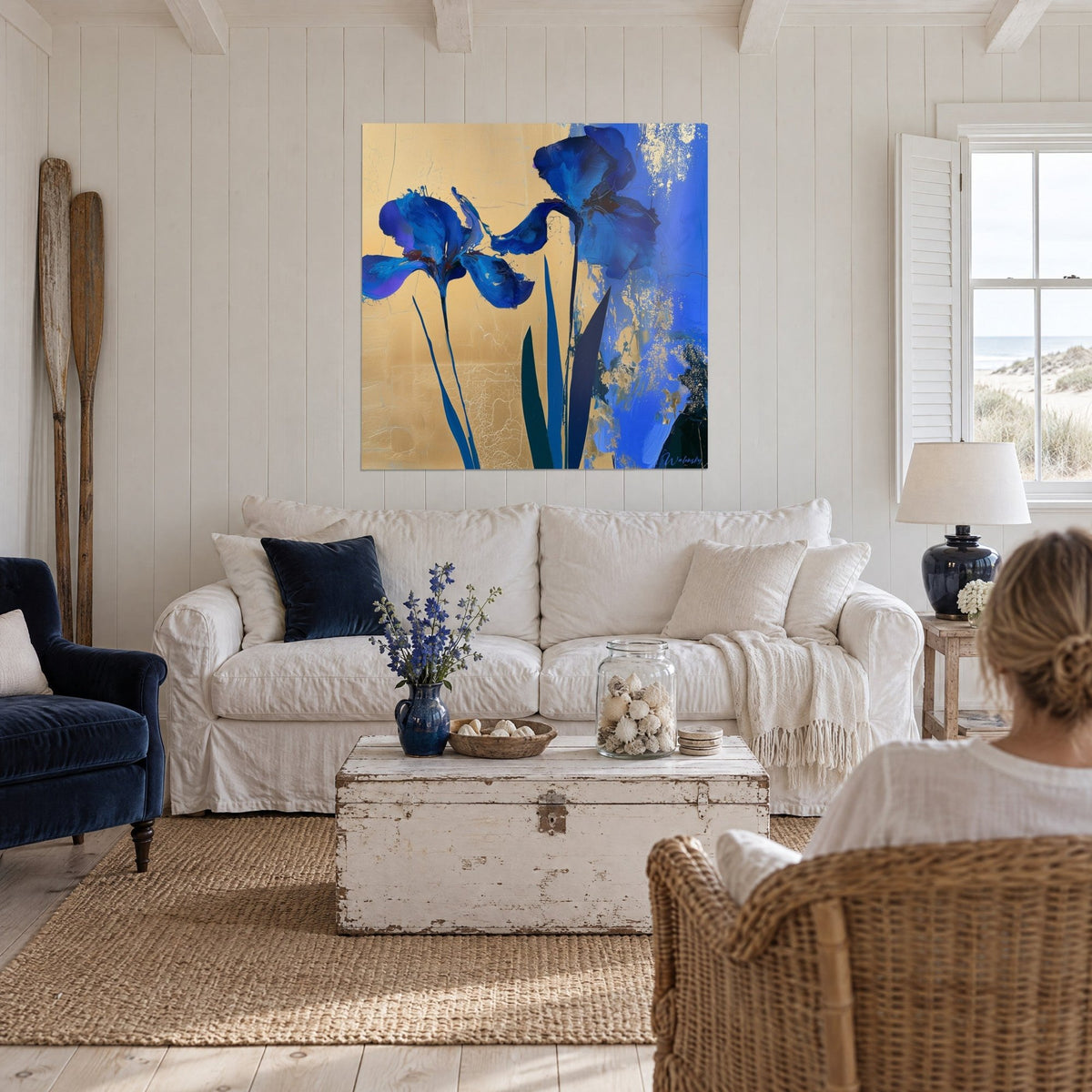 Wall art royal blue iris with crumpled petals on cracked gold background, dark green leaves, above a sofa in a bright living room