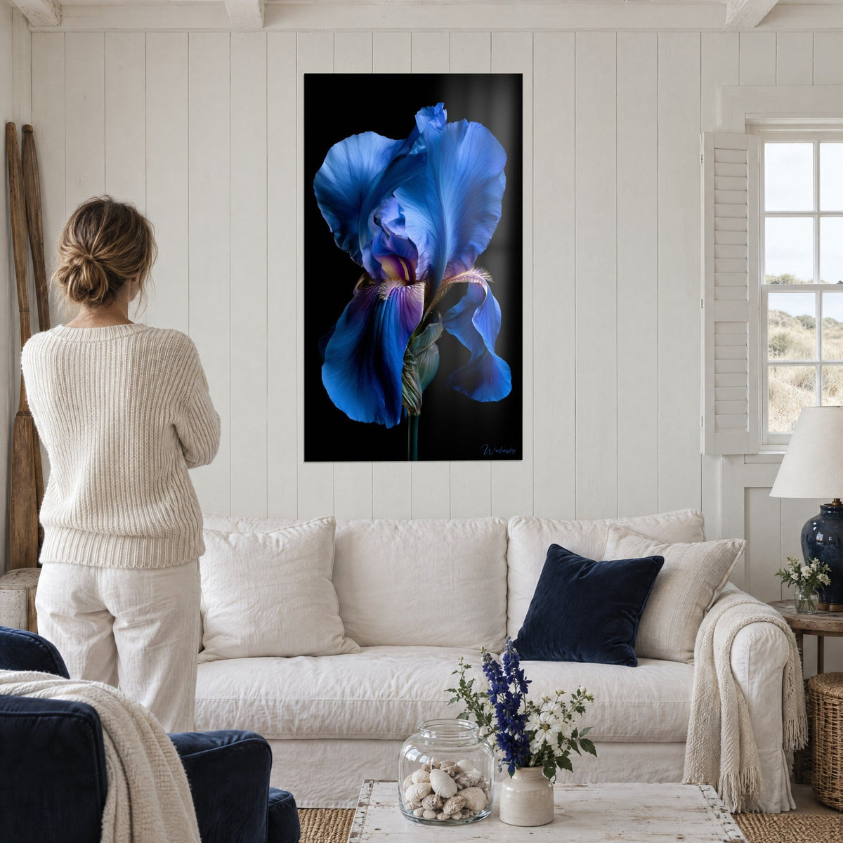 Wall art of a blue iris with crumpled petals on a black background, fuzzy golden beard, above a sofa in a bright living room