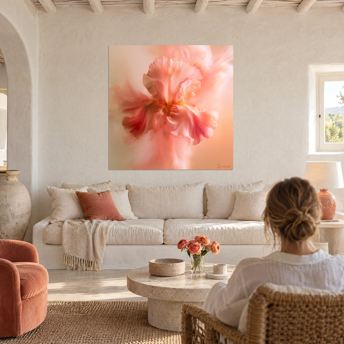 Cuadro de iris rosa coral con pétalos vaporosos y un brillo melocotón, una mujer de espaldas lo mira desde un sofá en un salón luminoso