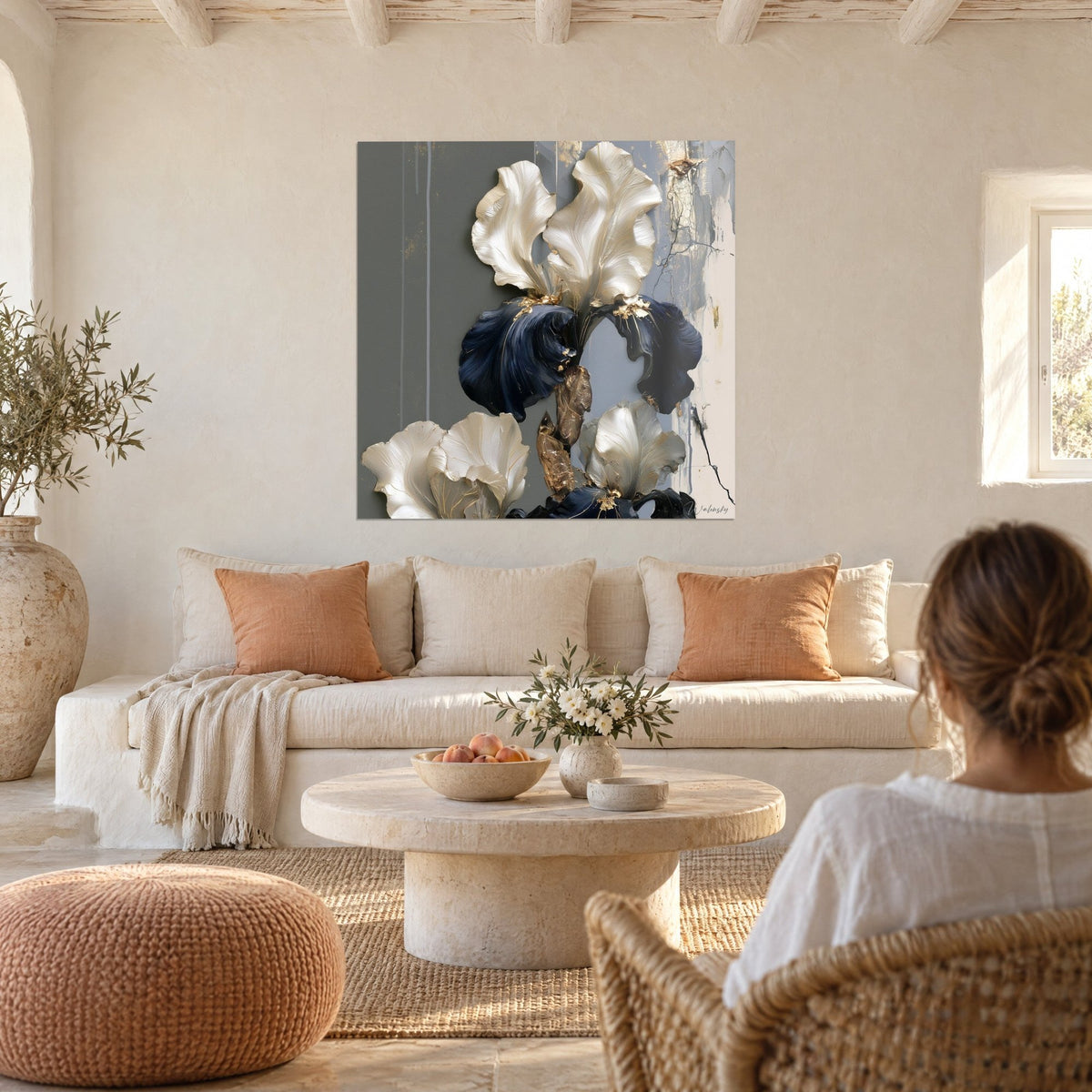 Quadro iris con petali avorio madreperlacei e corolle blu navy su fondo grigio, una donna di spalle, sopra un divano in un soggiorno luminoso