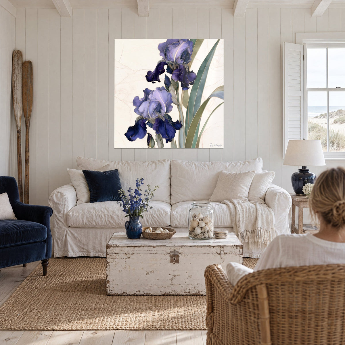 Wall art violet irises with wavy petals and gold outlines, sage green leaves, woman seen from behind, above a sofa in a bright living room