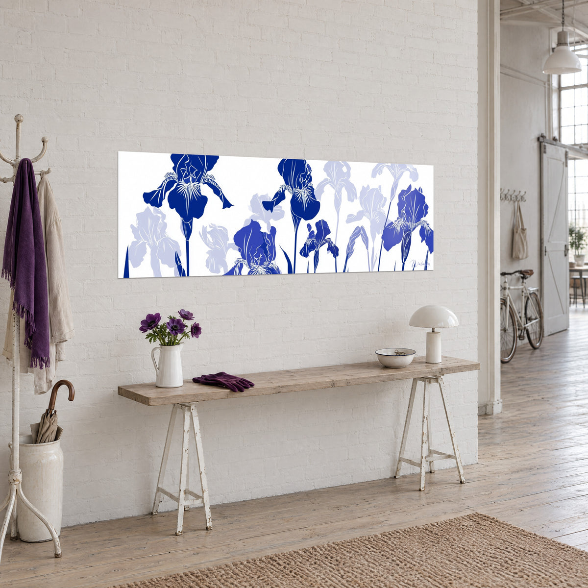 Cuadro con friso floral de iris índigo y lavanda de tallos esbeltos, colgado en una pared de ladrillo blanco junto a una consola