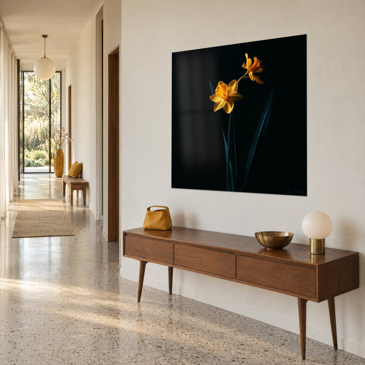 Wall art with amber jonquils and an orange bloom against an anthracite night, bluish stems, hung above a wooden sideboard in a hallway