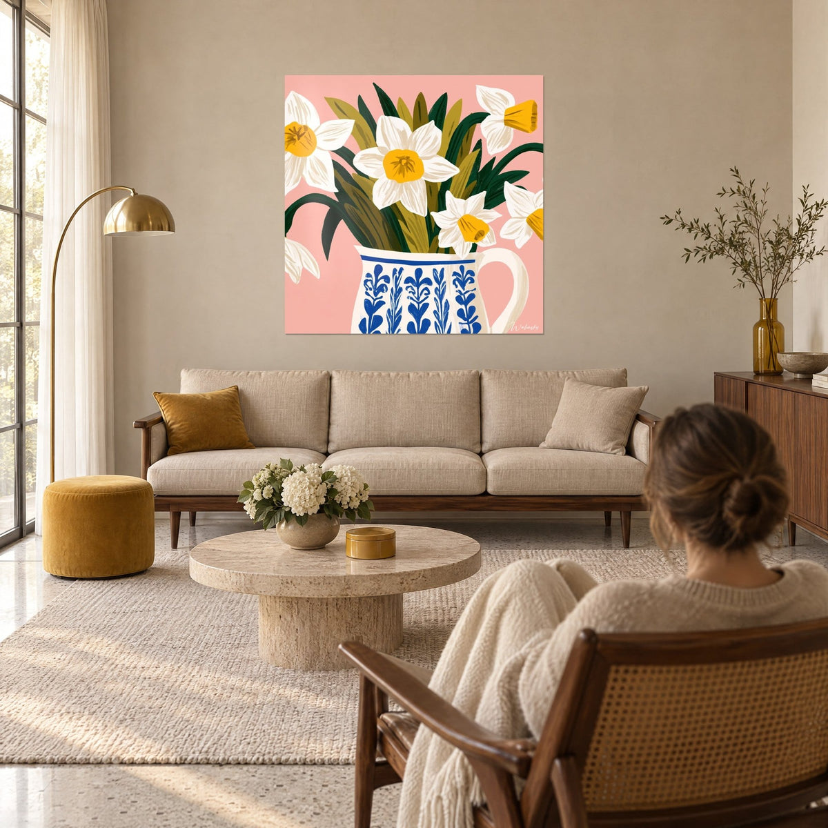 Tableau bouquet de jonquilles blanches à cœur jaune dans un pichet bleu et blanc, fond rose, au-dessus d'un canapé dans un salon lumineux