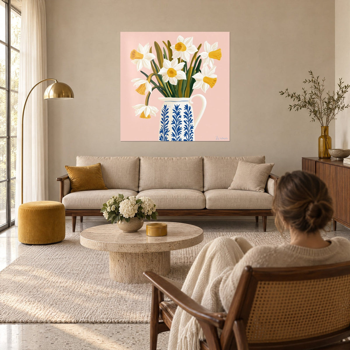Tableau bouquet de narcisses blancs au cœur jaune dans un pichet bleu et crème, fond rose, au-dessus d'un canapé dans un salon lumineux