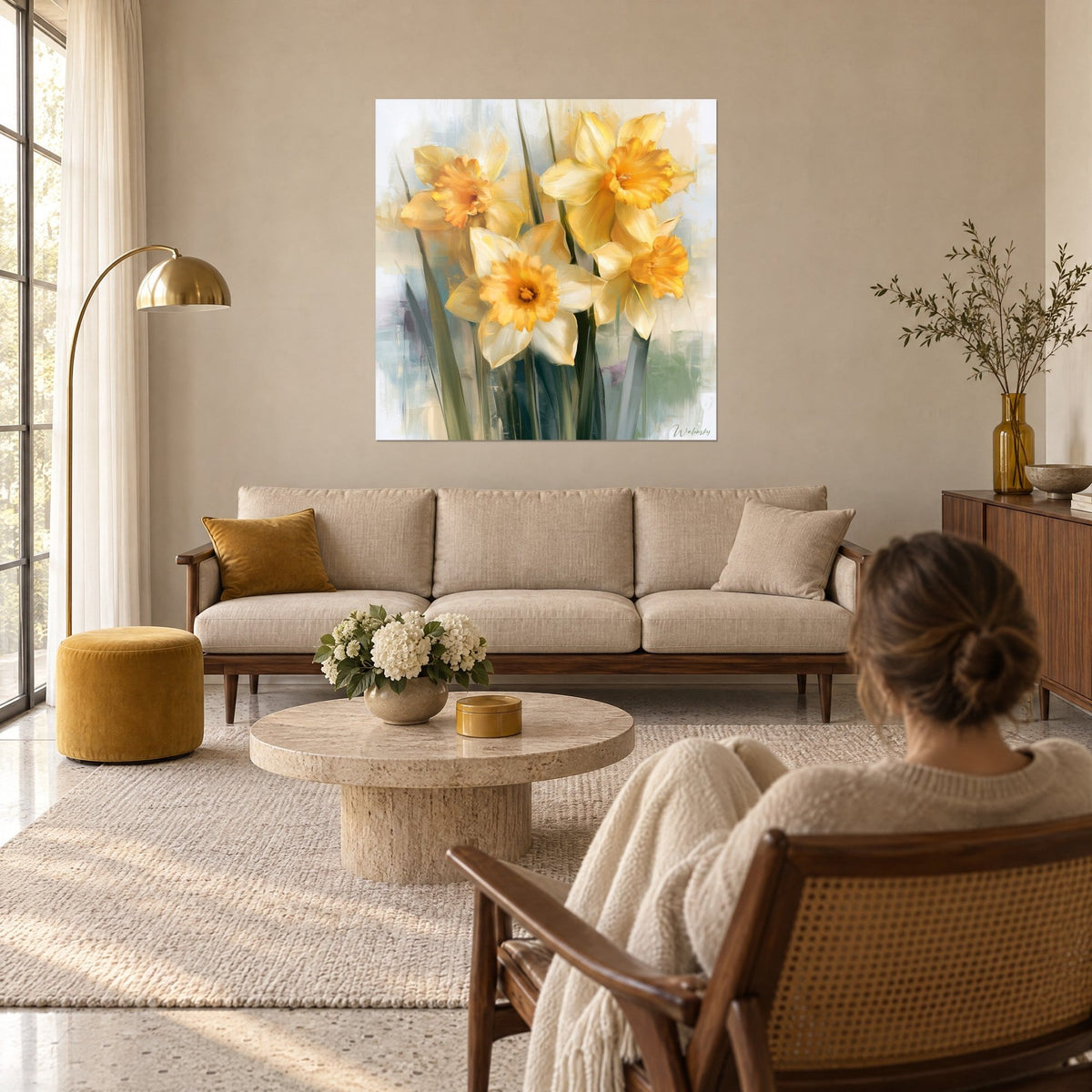 Quadro narcisi gialli a tromba arancione su sfondo azzurro pallido, una donna di spalle sopra un divano in un soggiorno luminoso