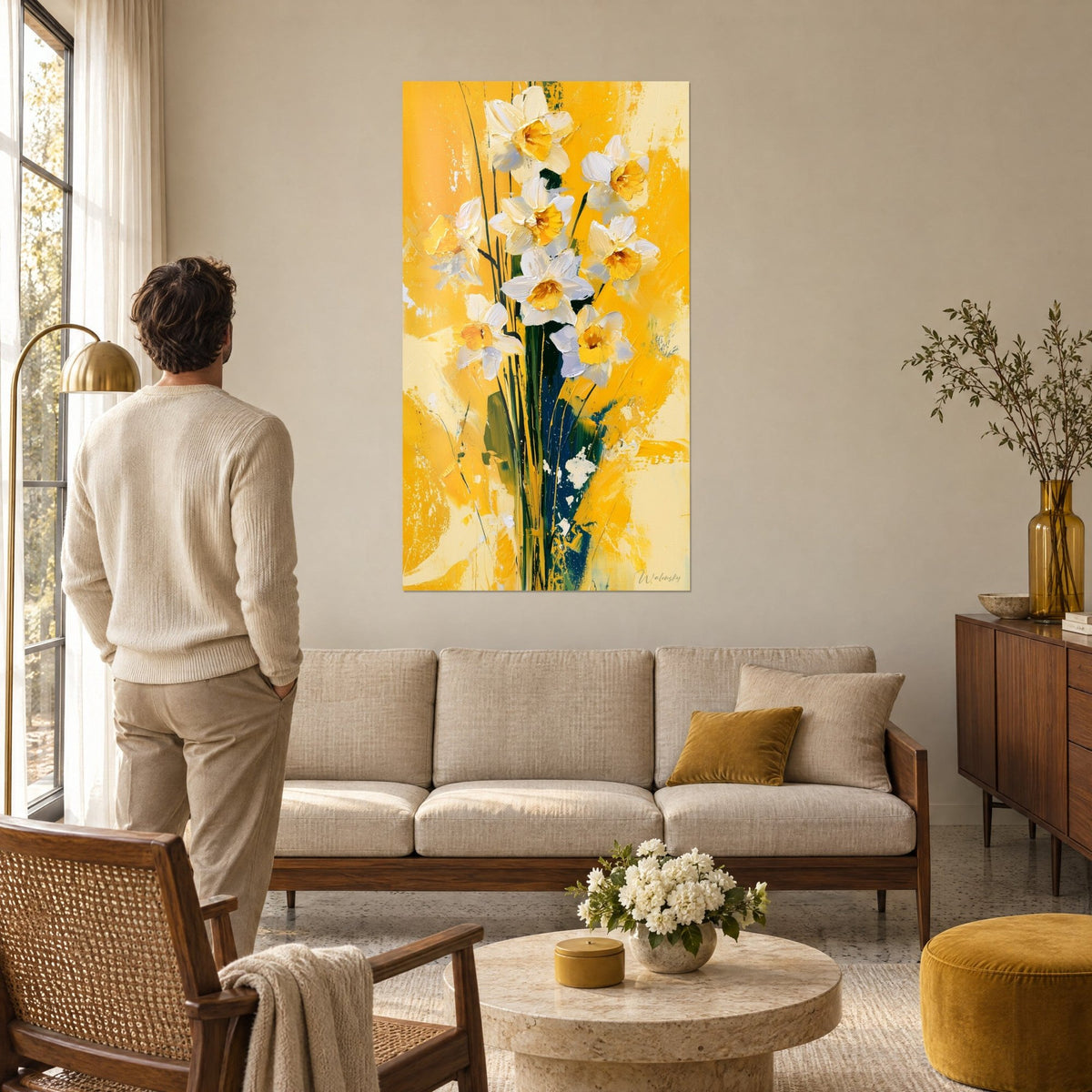 Quadro narcisi bianchi con cuori arancioni su fondo dorato, ammirato da un uomo con maglione color crema, sopra un divano in un soggiorno luminoso