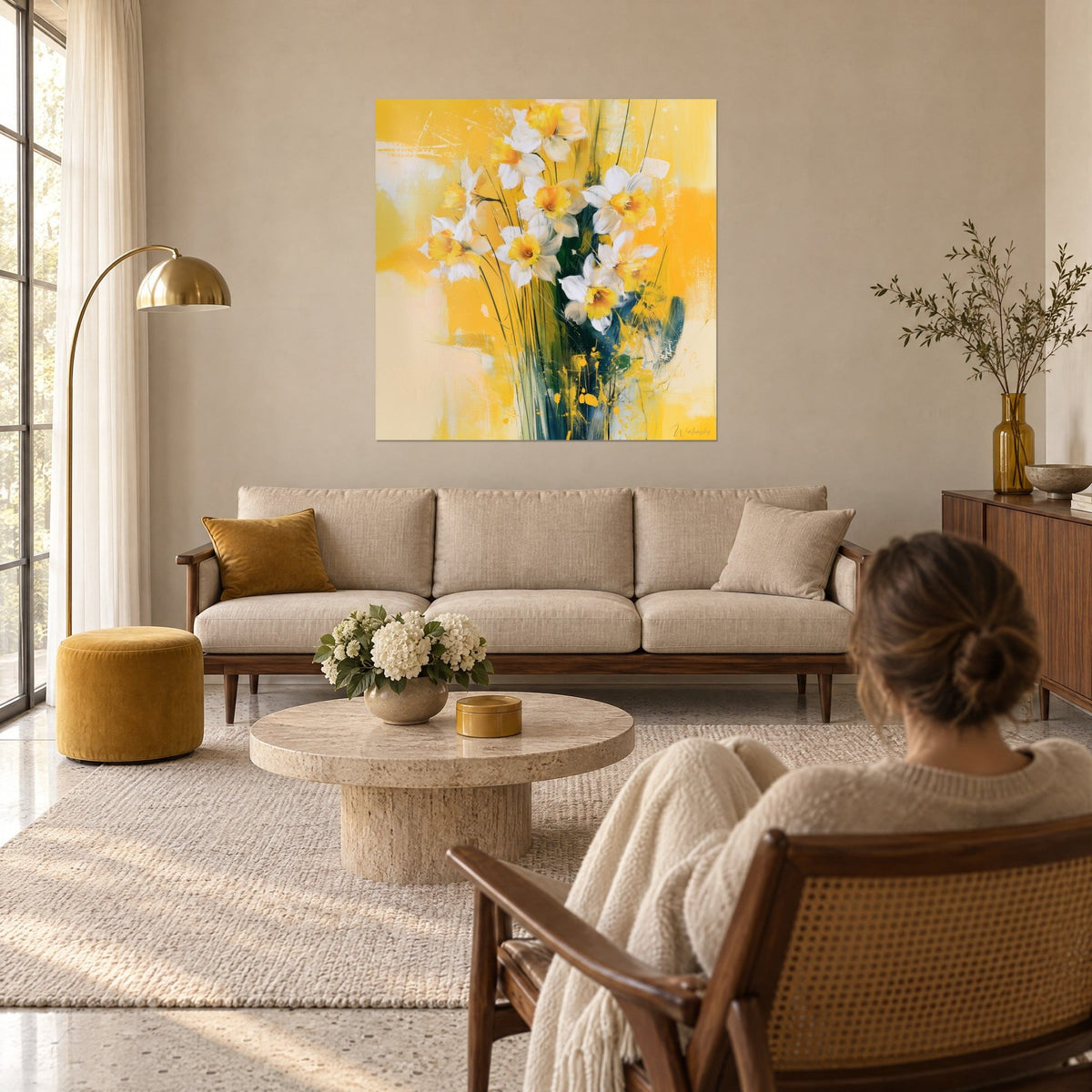 Cuadro de un ramo de narcisos blancos con corazón anaranjado sobre fondo amarillo mostaza, mujer de espaldas, encima de un sofá en un salón luminoso