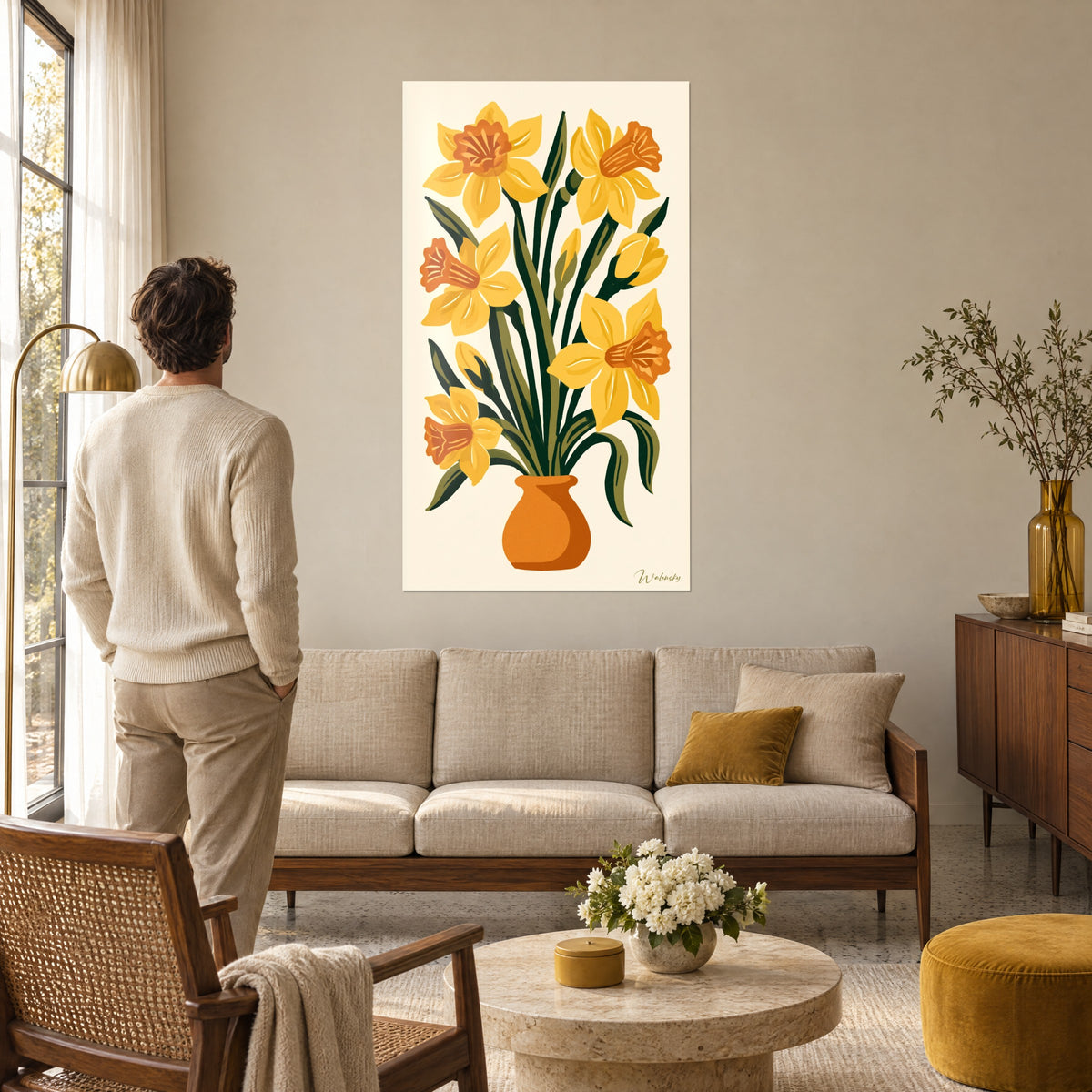 Cuadro con un ramo de narcisos amarillos en un jarrón naranja, hombre de espaldas en primer plano, sobre un sofá en un salón luminoso