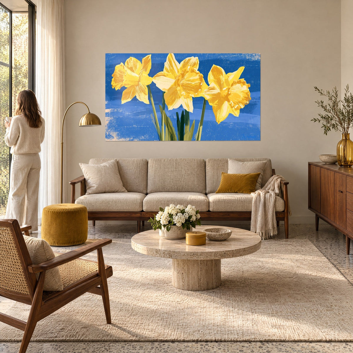Quadro tre narcisi dorati su fondo blu cobalto sfumato, steli verdi, donna di spalle sopra un divano in un soggiorno luminoso