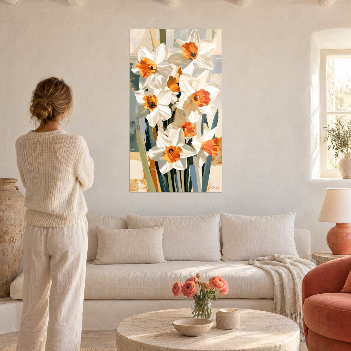 Wall art white daffodils with orange centers, slate blue stems, woman seen from behind, above a sofa in a bright living room