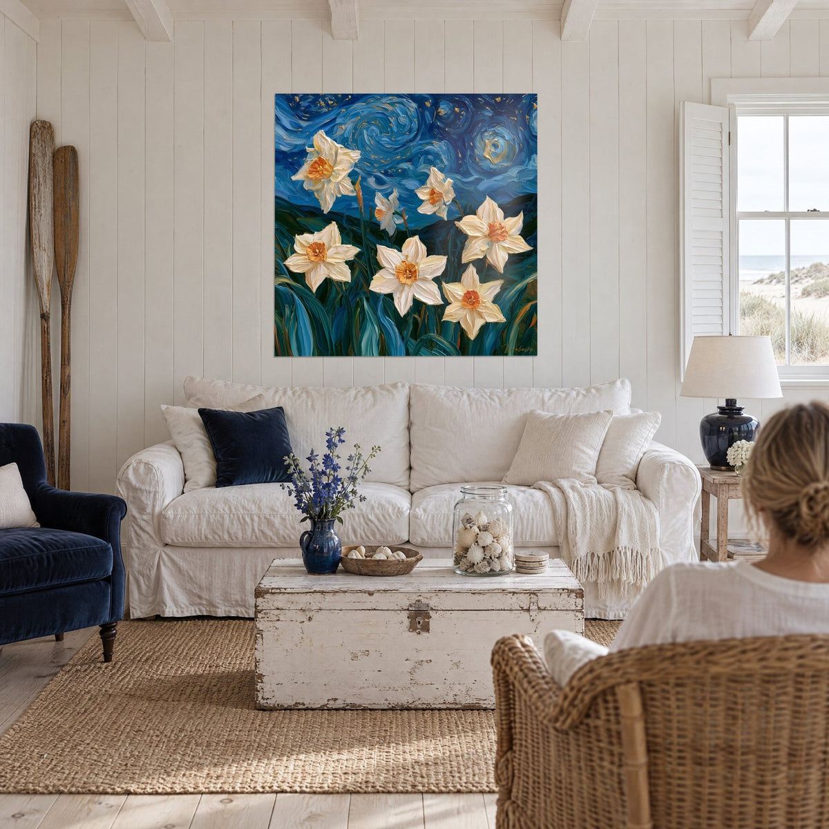 Wall art of white daffodils with orange centers under a swirling blue sky, hung above a sofa in a bright living room