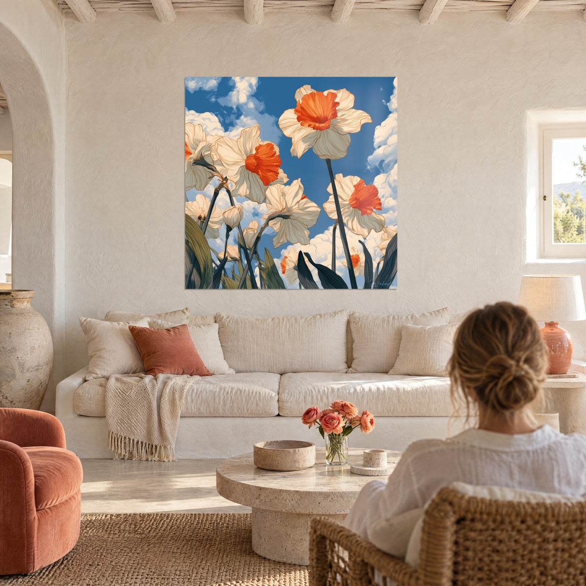 Schilderij van ivoorkleurige narcissen met fel oranje hartjes, van onderaf gezien tegen een blauwe lucht, vrouw met de rug naar de kijker boven een bank in een lichte woonkamer