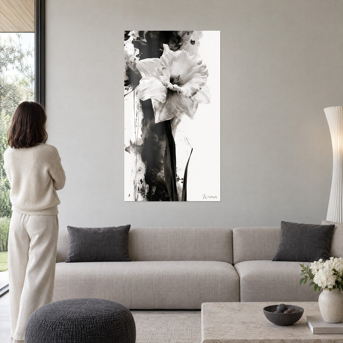 Wall art of white ruffled daffodil, black stem and ink splatters, hung above a sofa in a bright living room