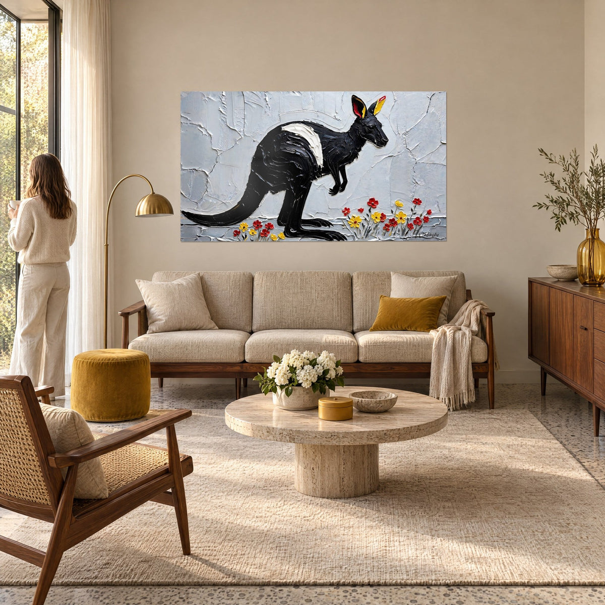 Tableau kangourou noir à la tache blanche, oreilles jaunes et rouges, fleurs en relief, au-dessus d'un canapé dans un salon lumineux