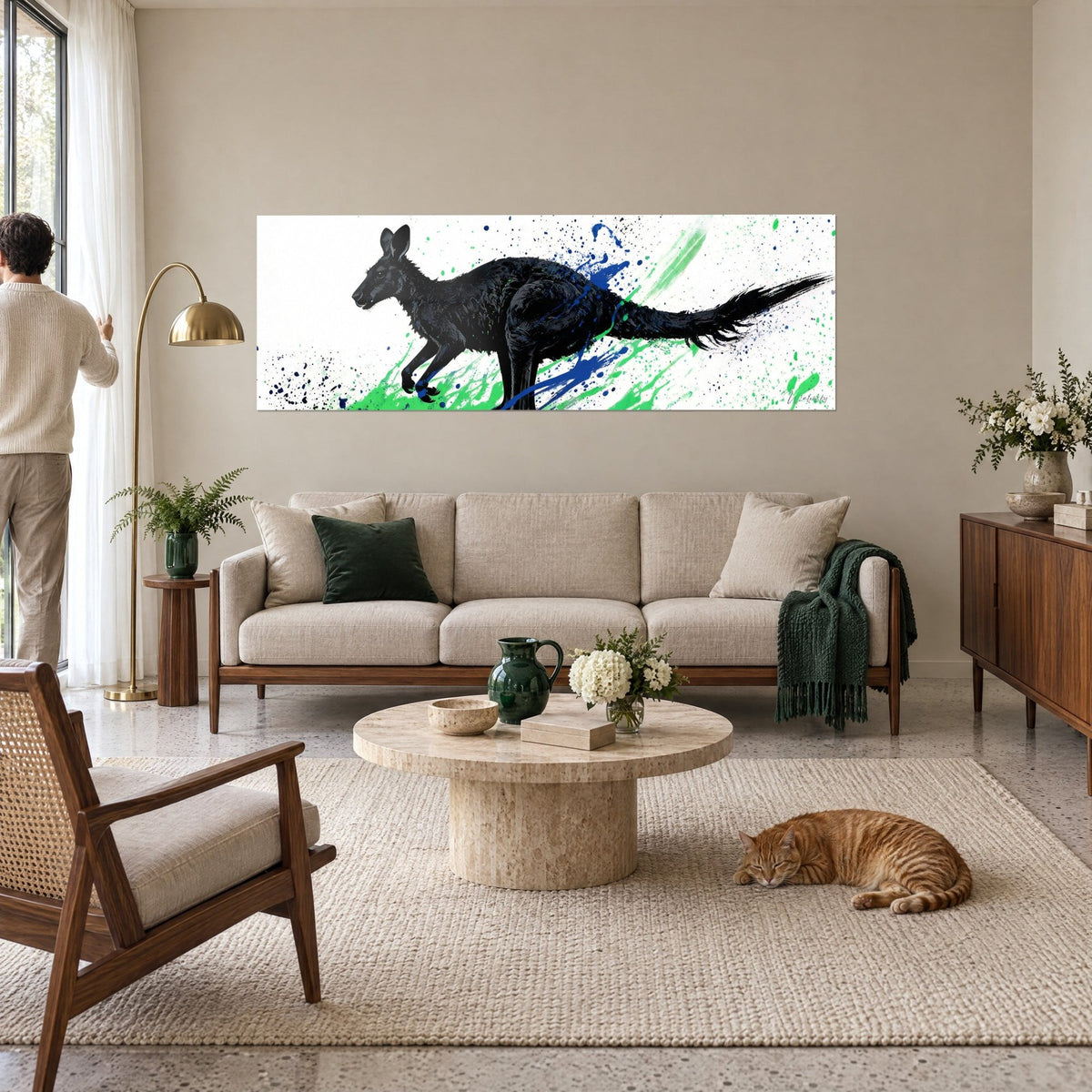 Cuadro Canguro negro saltando, salpicaduras verdes y azules sobre fondo blanco, encima de un sofá en un salón luminoso