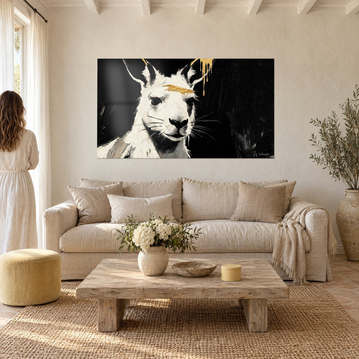 Tableau kangourou blanc aux oreilles dressées, coulure dorée sur le front, fond noir, femme de dos, au-dessus d'un canapé dans un salon lumineux