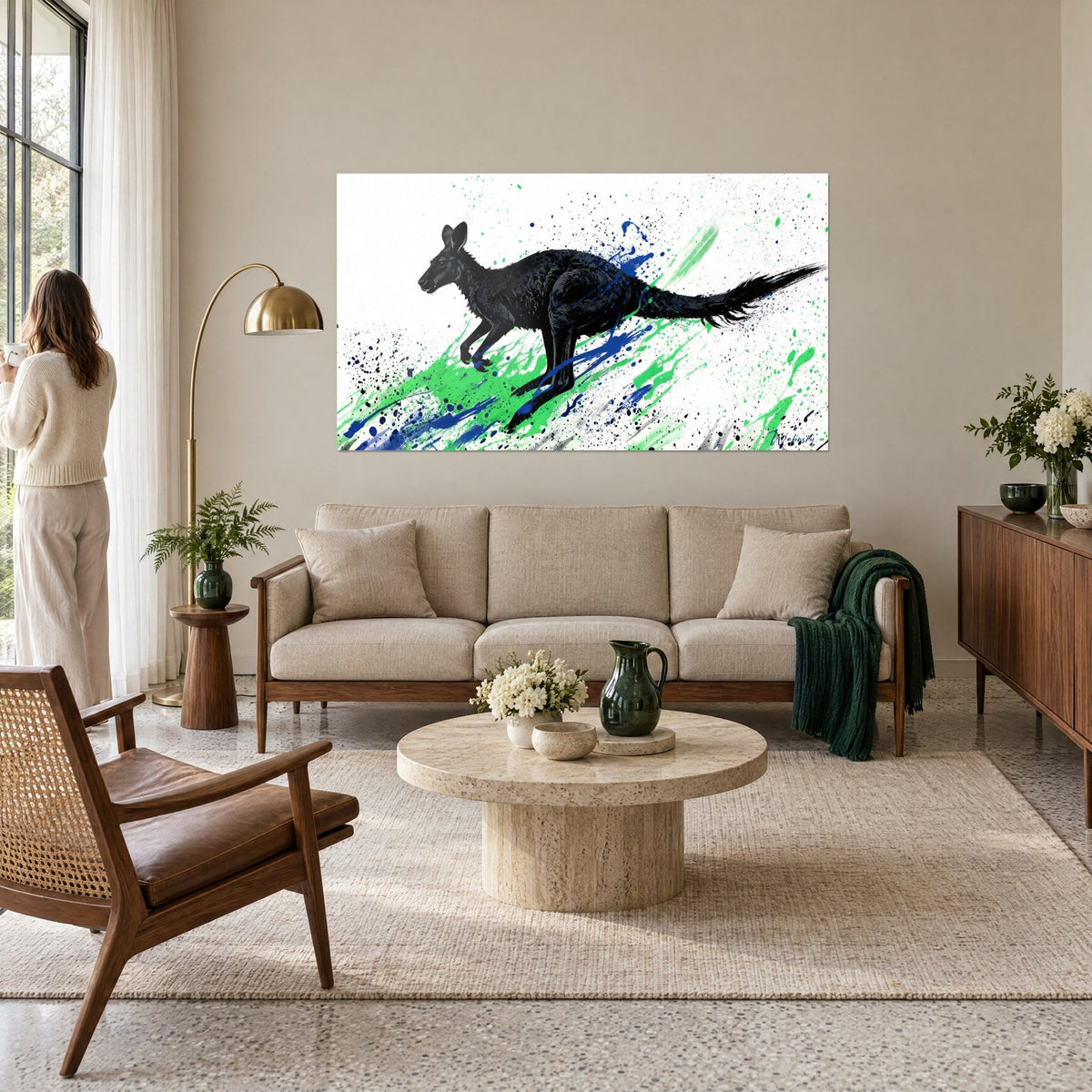 Tableau kangourou noir bondissant, éclaboussures vertes et bleues sur fond blanc, au-dessus d'un canapé dans un salon lumineux