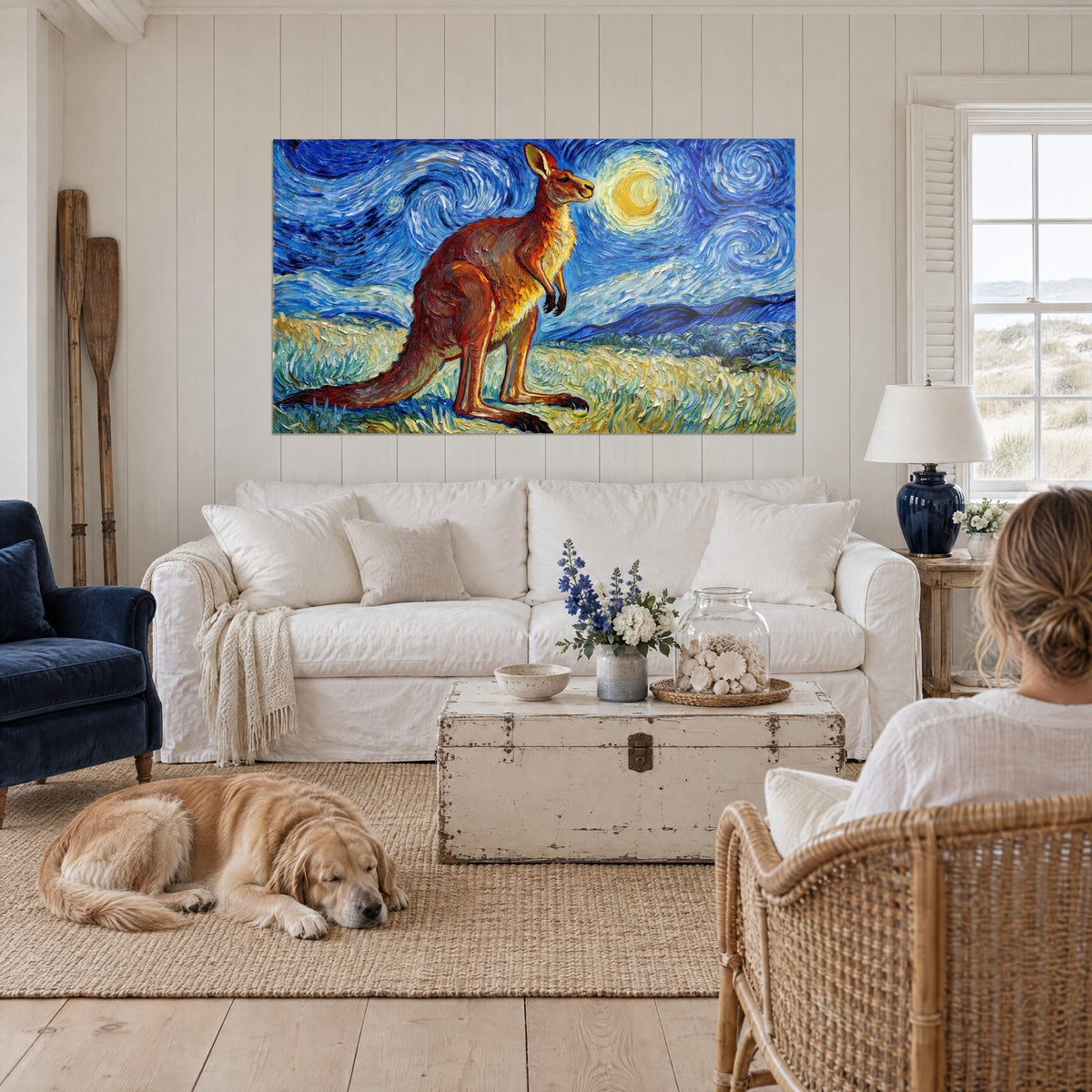 Wall art of a rust-red kangaroo standing upright under a swirling blue sky, yellow moon, a person and a retriever above a sofa in a bright living room