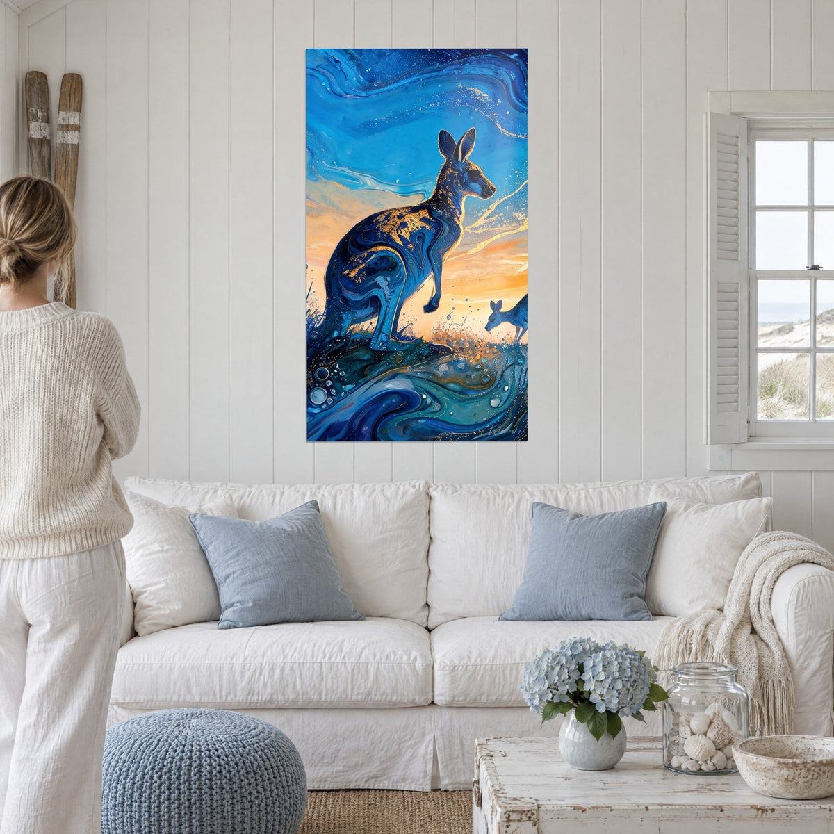 Tableau kangourou bleu cobalt aux éclats dorés, ciel orangé de fin de jour, au-dessus d'un canapé dans un salon lumineux