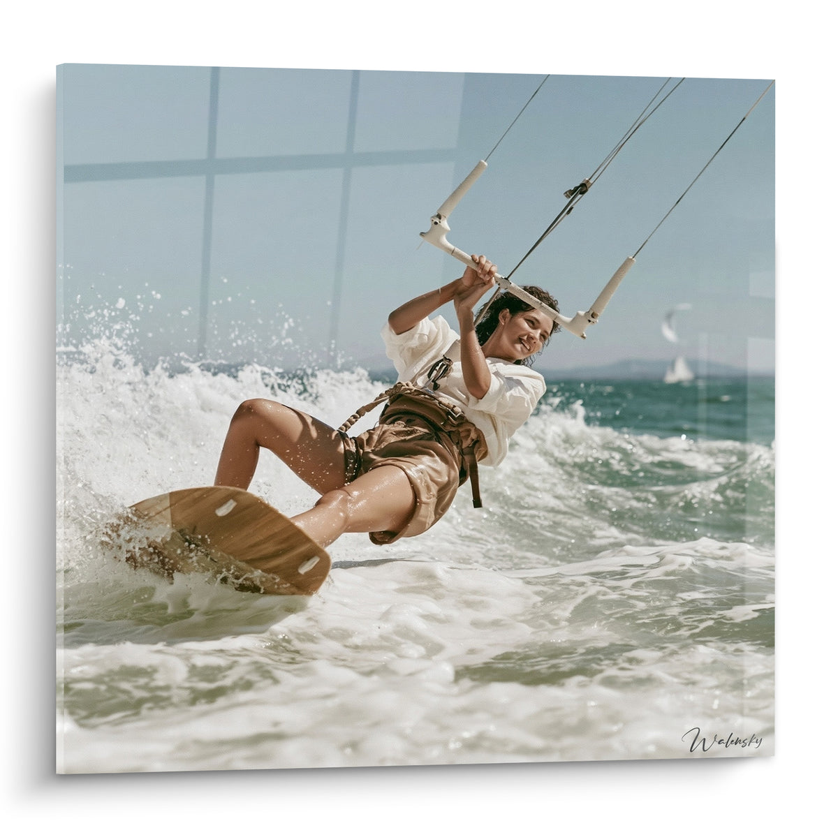 Kitesurfeuse penchée sur planche ocre, écume blanche et ciel bleu pâle éclatant