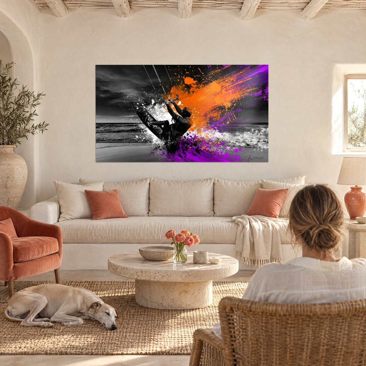 Schilderij kitesurfer midden in de sprong op grijze achtergrond, oranje en violette spatten, vrouw van achteren en windhond boven een bank in een lichte woonkamer