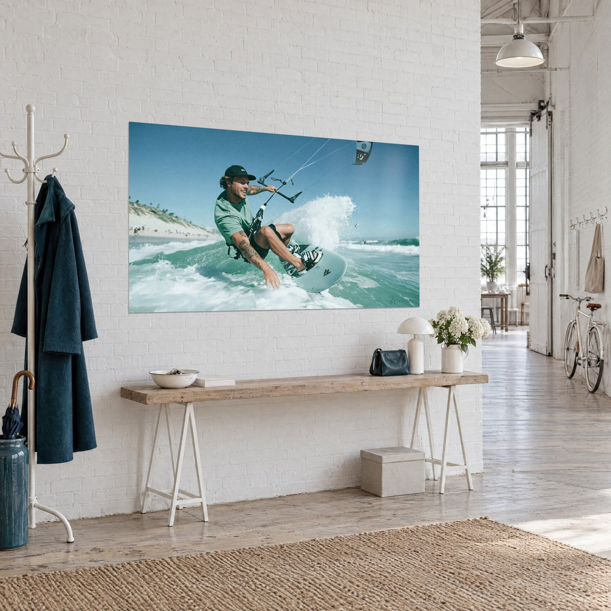 Tableau sportif de glisse barbu et tatoué, sourire aux lèvres, planche gris-vert fendant la vague turquoise, mur de briques blanches d'un loft